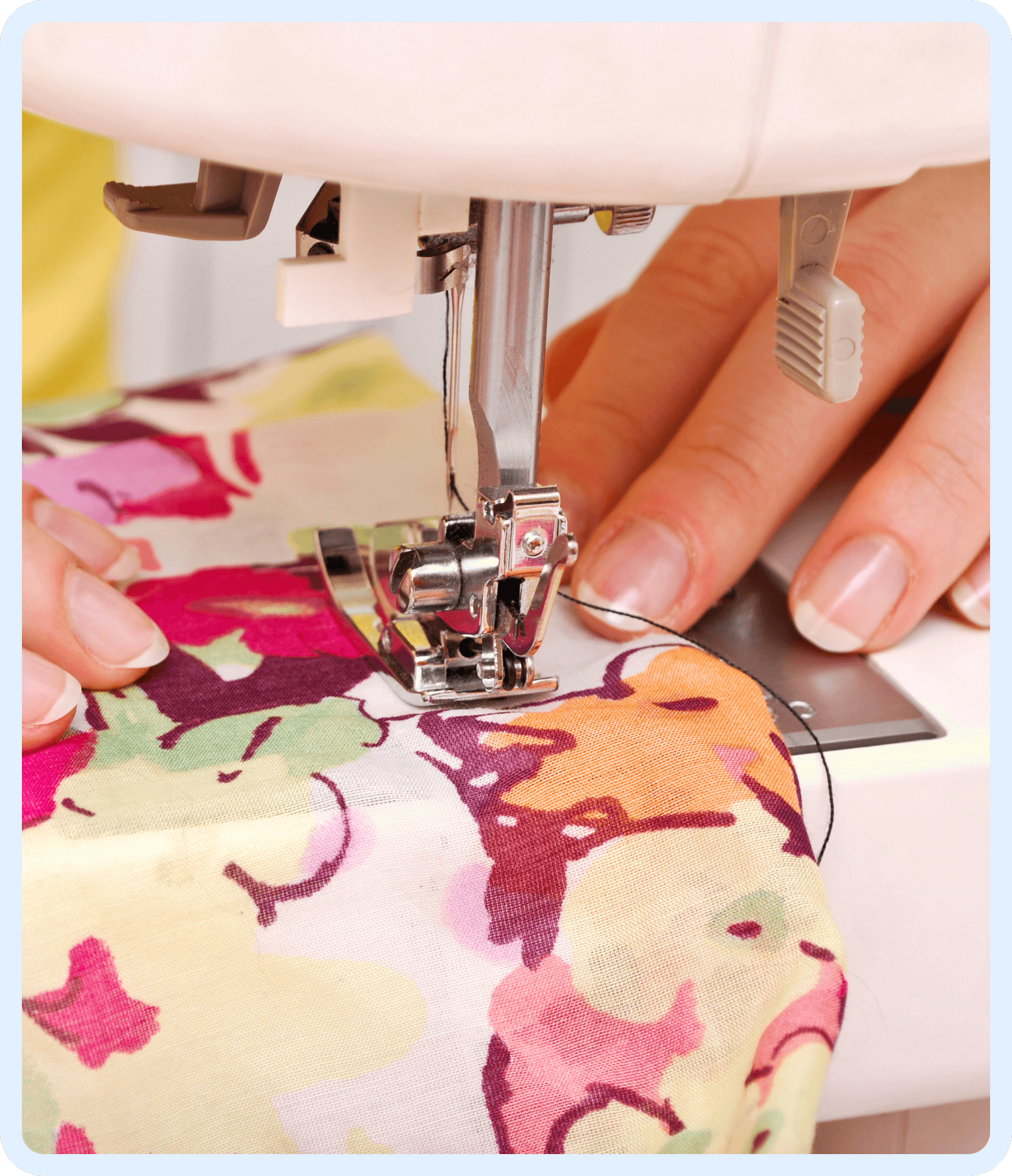 Close-up of hands guiding a colorful floral fabric through a sewing machine, with a needle and presser foot in focus.